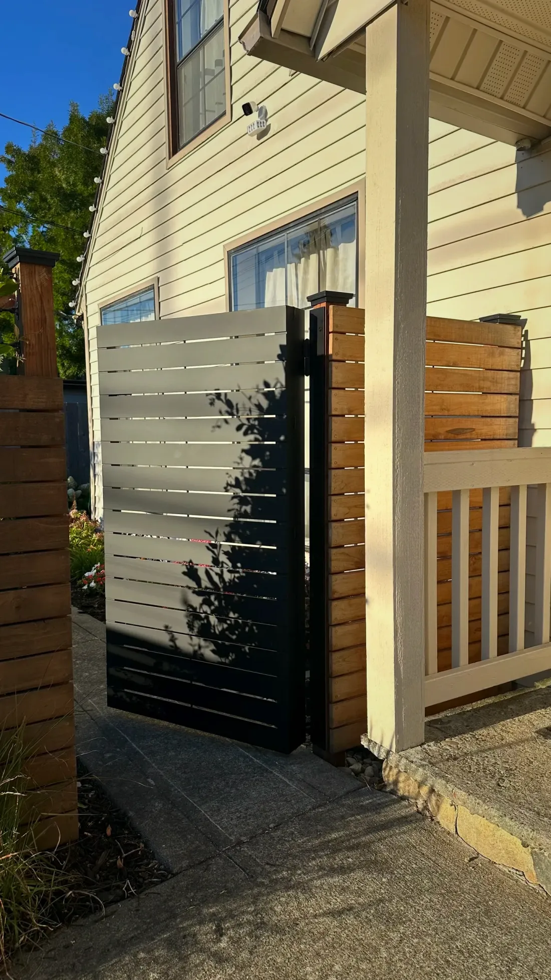 Powder-coated aluminum privacy gate with horizontal slats beside a cedar fence